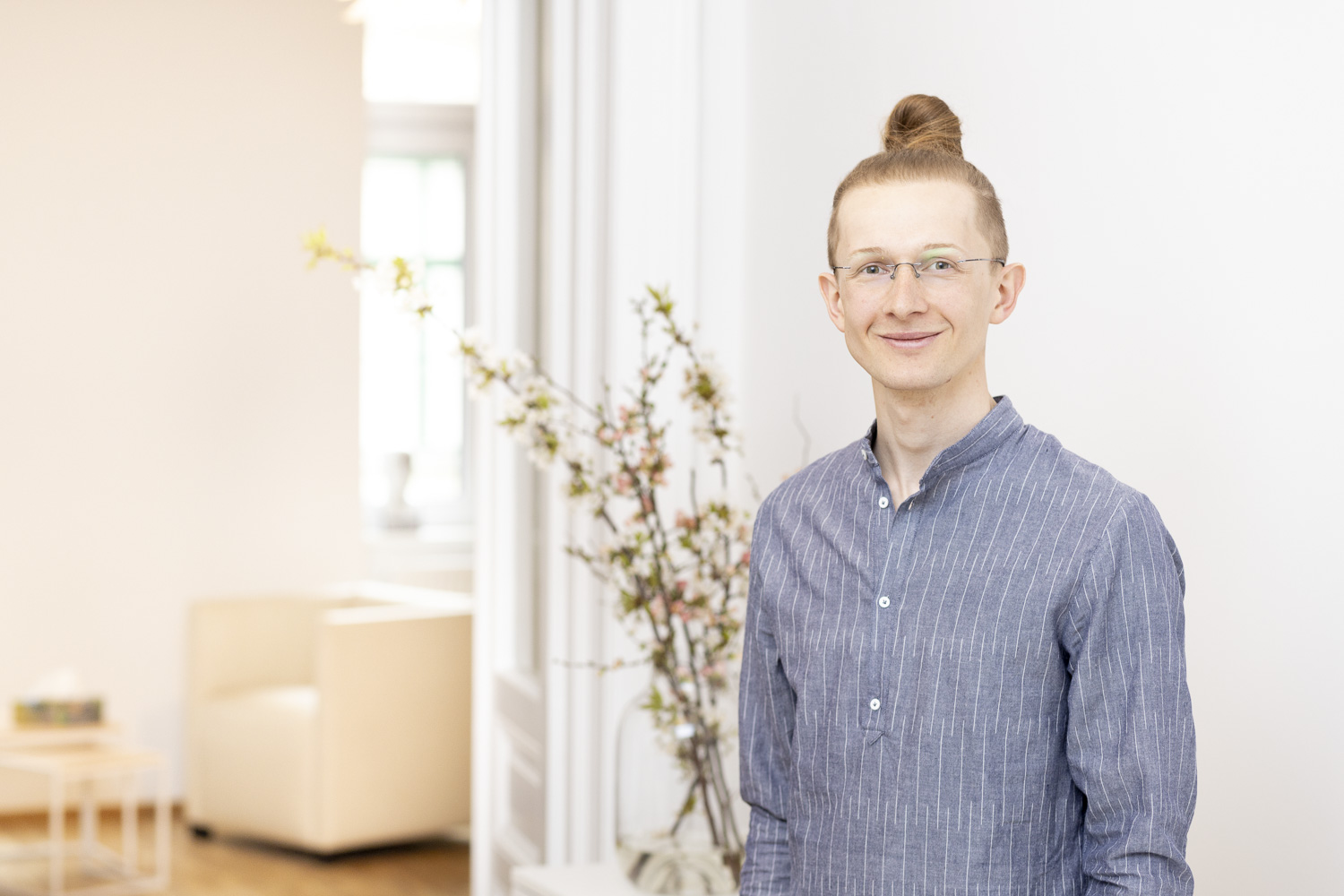 Businessportrait in Psychotherapiepraxis in Wien, Person steht rechts im Bild und lächelt leicht, im Hintegrund ist ein Praxisraum zu sehen