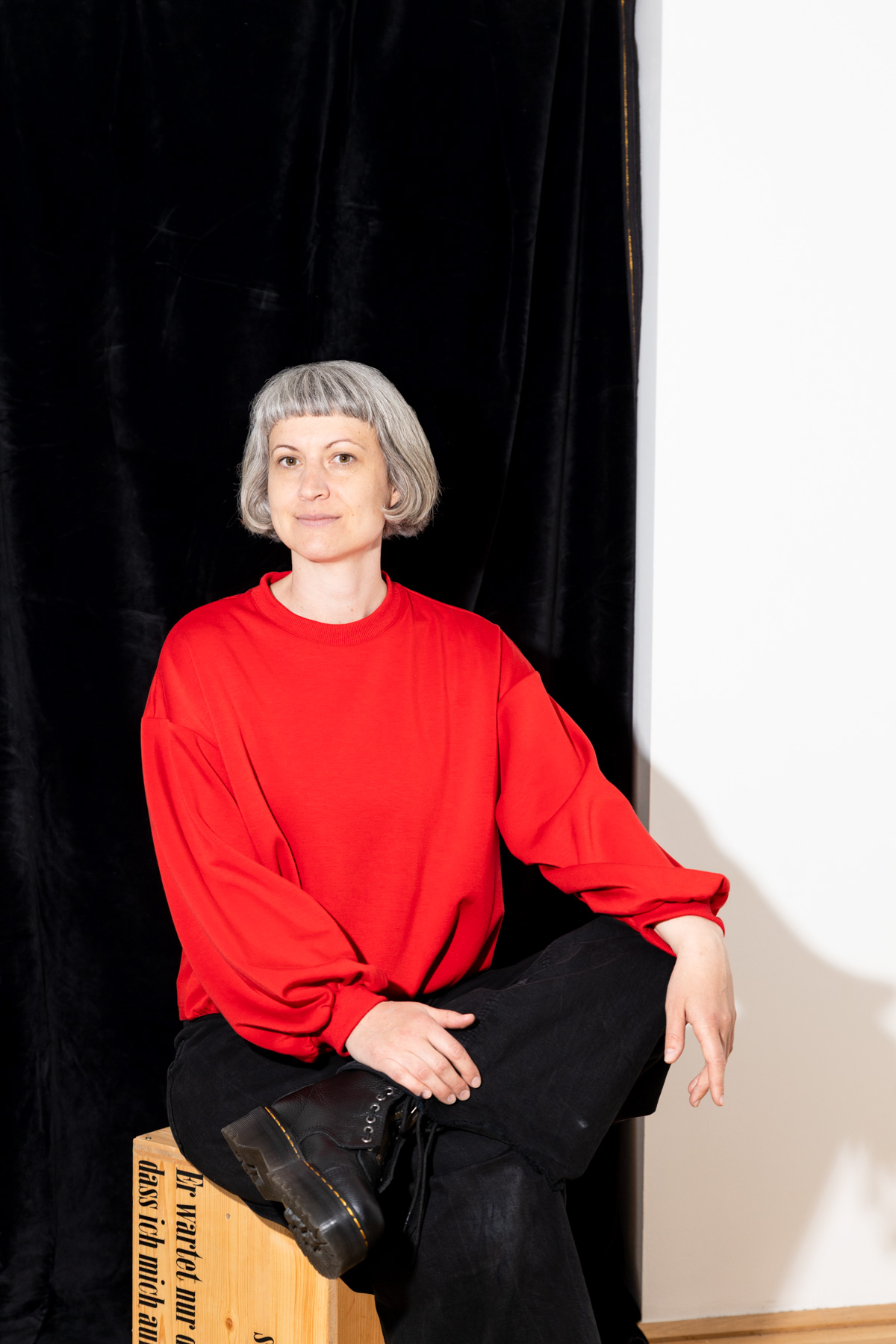 Portraitfotografie einer Kostuembildnerin, hartes Licht, Frau sitzt vor halb schwarzem, halb weißem Hintergrund, in ihrem Atelier in Wien