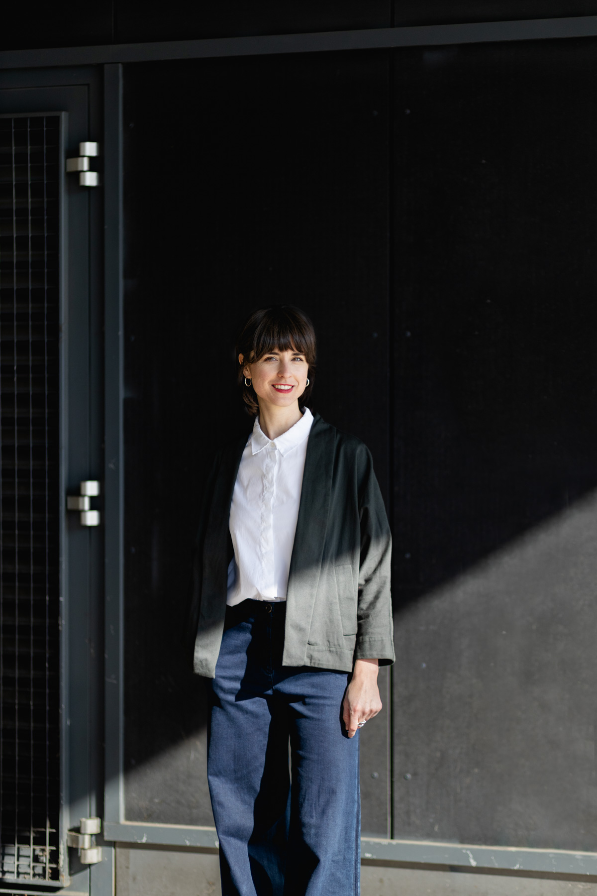 Portrait einer Stadtforscherin, Farbfotografie, Person steht vor einer dunklen Wand, ein starker Schatten verläuft schräg durch das Bild